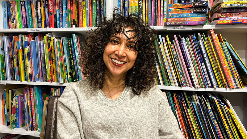 Radha Chakraborty smiling while sitting in front of shelves of children's books