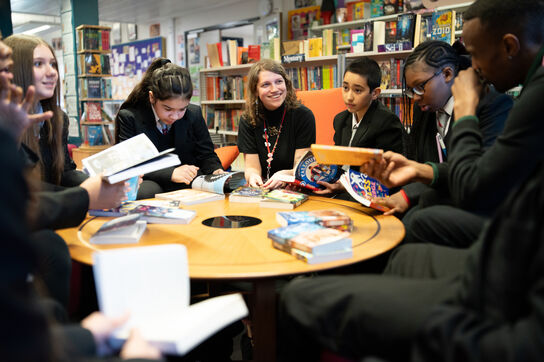 A group of secondary school students gathered around a library table, talking about their Bookbuzz Secondary books.