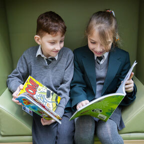 two children sitting on a green sofa chair with Bookbuzz Primary books