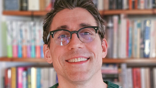 Tom Percival smiling in front of bookshelves