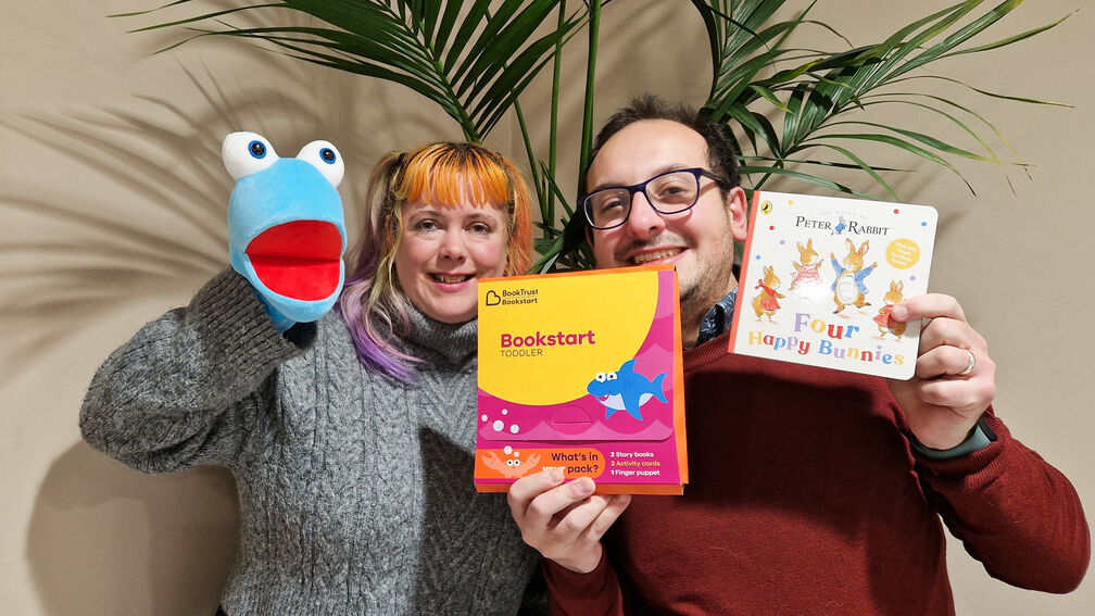 two people facing the camera and posing at the camera holding up a puppet and books