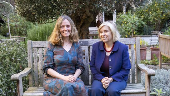 Annie Crombie and Diana Gerald sitting together on a bench in a garden, smiling at the camera.