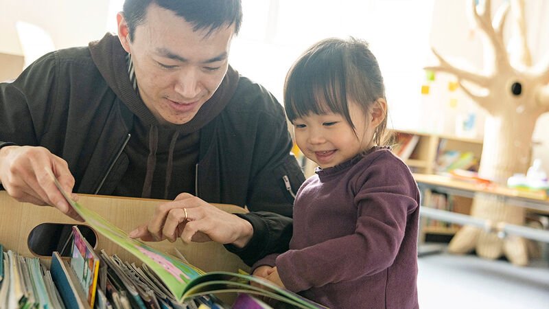 A father and a daughter smiling while looking at books together