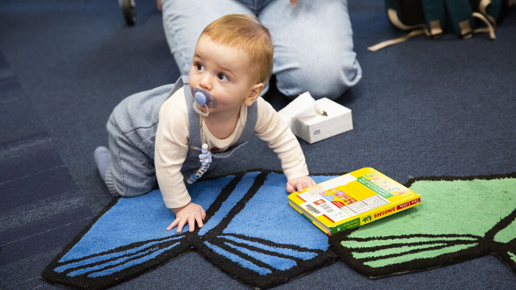 A baby with a dummy is crawling on the floor among books in a library setting