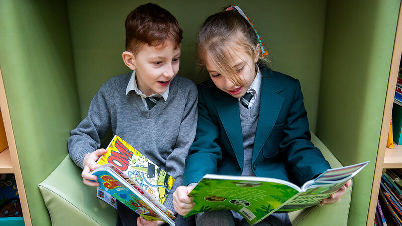 A primary aged boy and girl sitting in a high-walled chair looking at books together