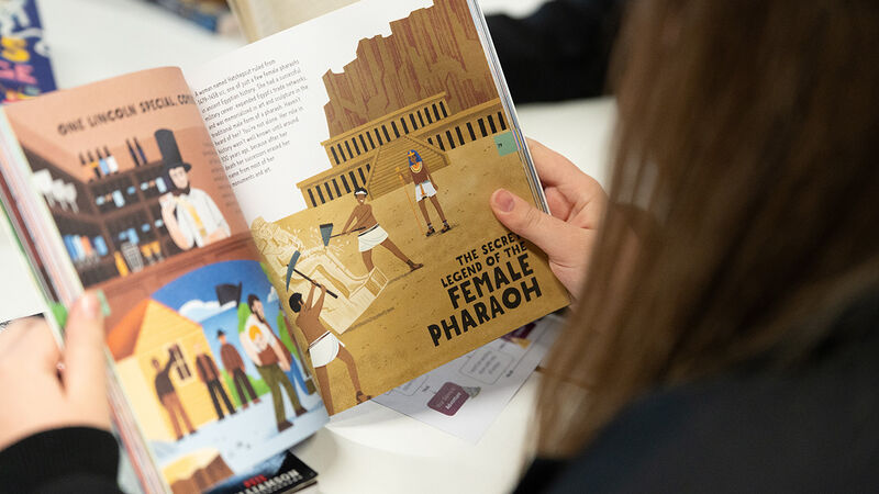 A girl looking at an illustrated book - the photo is taken over her shoulder