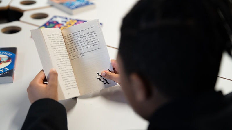 A boy sitting at a desk reading - the photo is taken over his shoulder