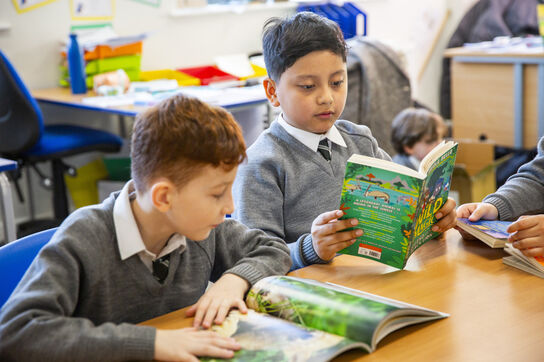 Two primary school boys in school uniform sitting together at a desk, reading