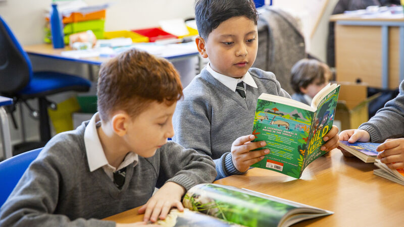 Two primary school boys in school uniform sitting together at a desk, reading