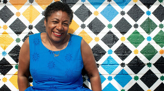 Waterstones Children's Laureate Patrice Lawrence smiling as she sits in front of a wall painted in colourful diamonds