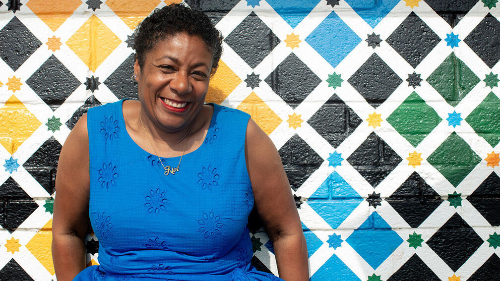 Waterstones Children's Laureate Patrice Lawrence smiling as she sits in front of a wall painted in colourful diamonds