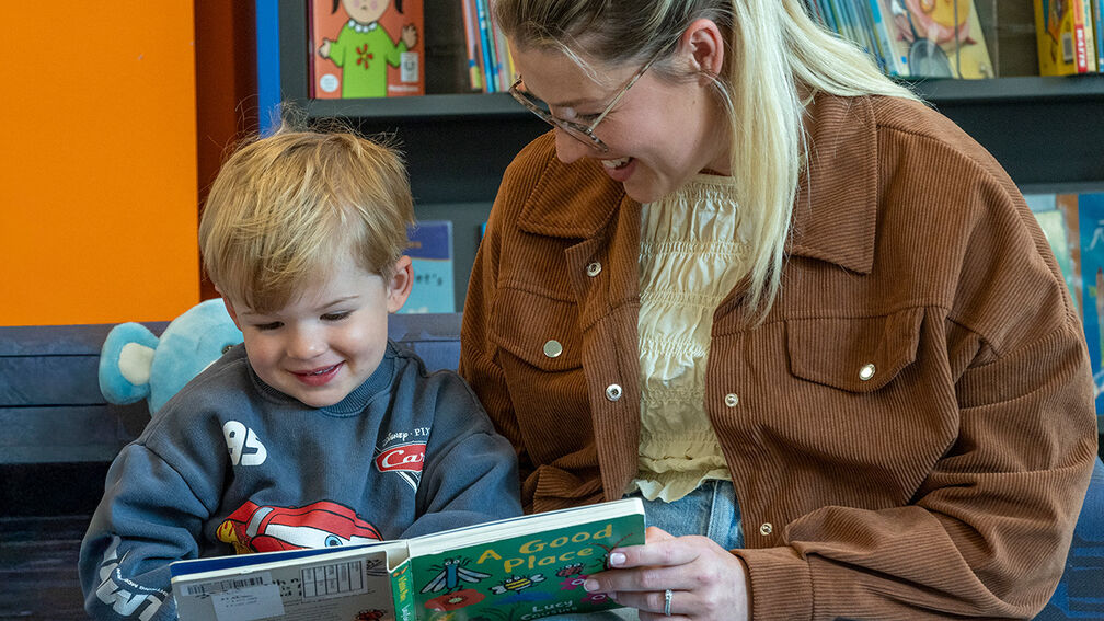 A woman and a child laughing as they look at a book together in a library