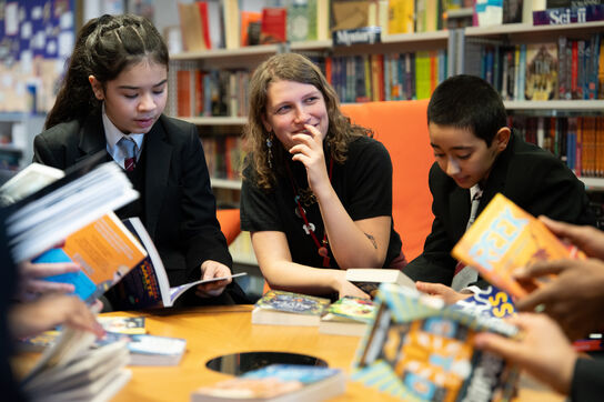 A school librarian reading with secondary school children in a library