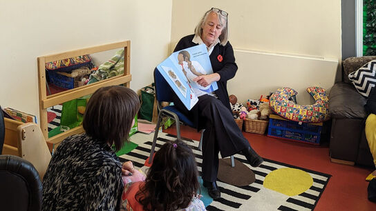 Families listening to a storyteller holding a book for them to see.