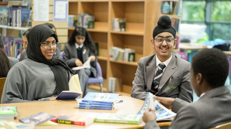 A girl and two boys aged 12 are reading together in a school library and smiling