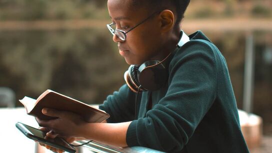 Young person with a book and a phone in their hand (Represents newsletter)