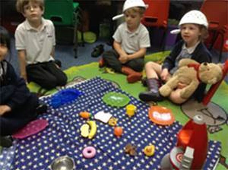 Children sitting round a picnic, two wearing colanders on their head and one holding a teddy