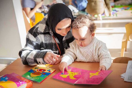 A woman wearing a hijab looking at a book with baby.