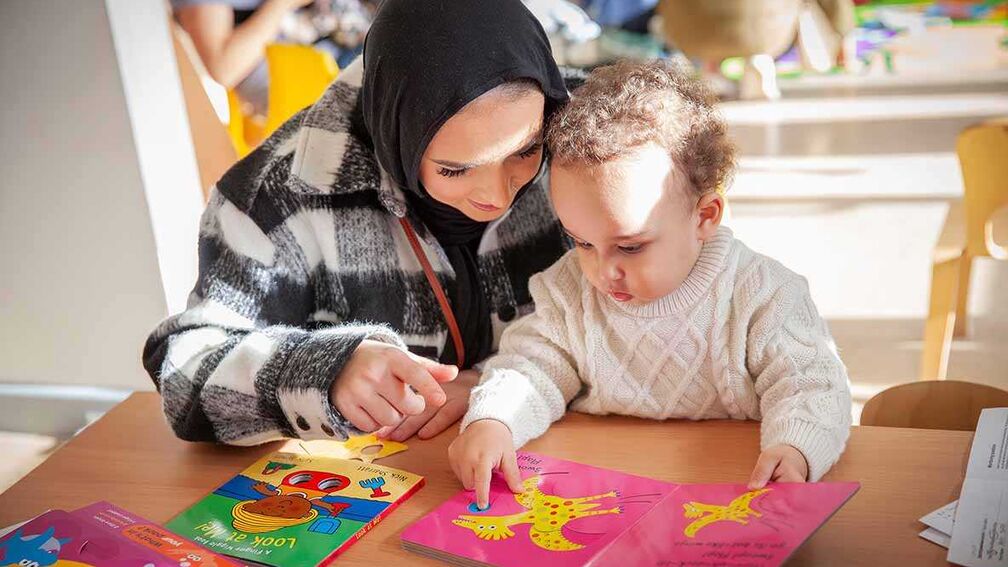 A woman wearing a hijab looking at a book with baby.