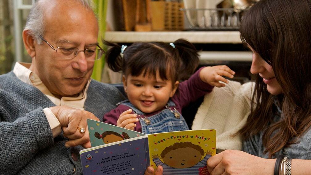 A grandparent and mother supporting the reading of a child.