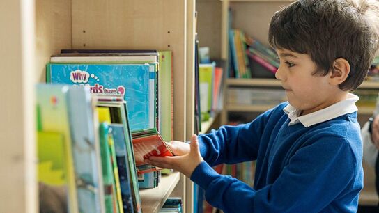 A boy in school uniform choosing a book from the shelf.