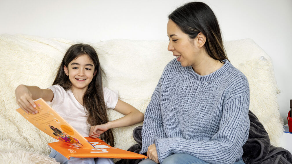 A smiling girl opening a Letterbox Club pack while sitting next to a woman