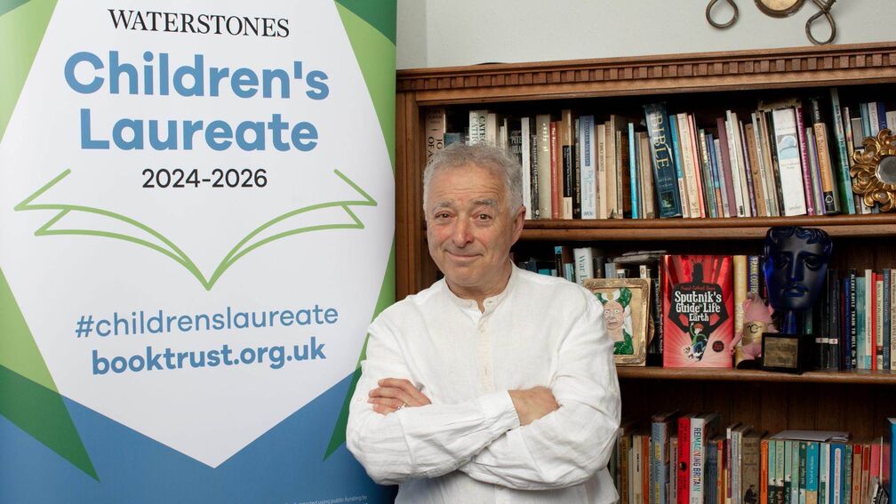 frank cottrell boyce standing next to banner stand and books