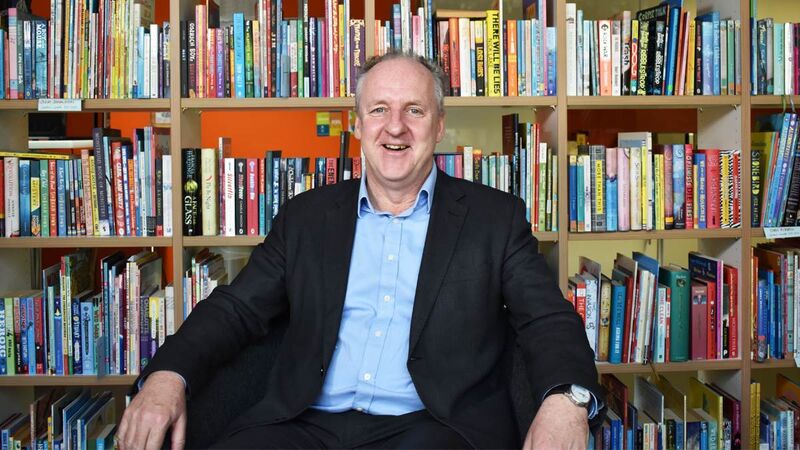 John sitting in a chair in front of a bookshelf, smiling.