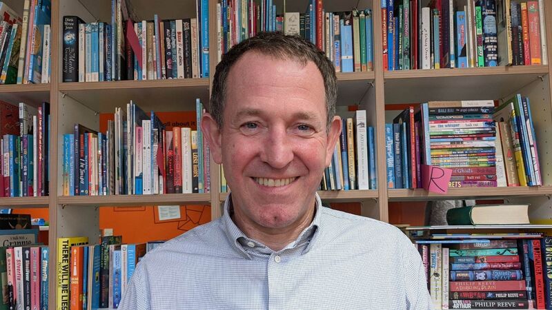 Nigel looking to camera and smiling with books in the background.