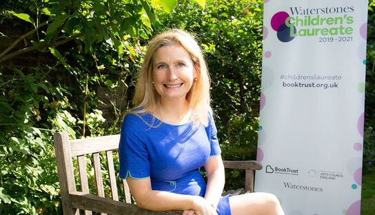 Cressida Cowell sitting on a park bench, smiling.