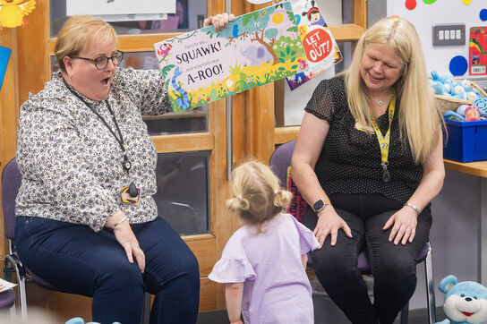 Two Storytime practitioners reading to a young child.