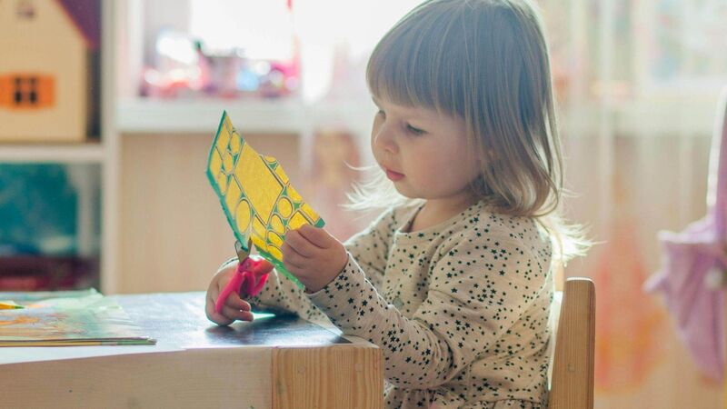 A girl in nursery cutting out a paper shape.