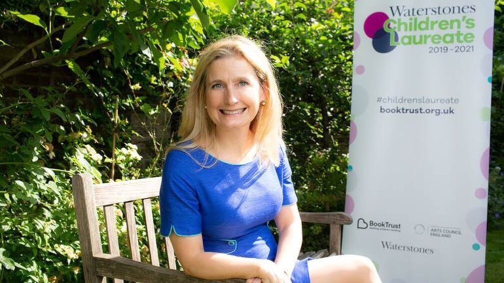 Cressida Cowell sitting on a park bench, smiling.