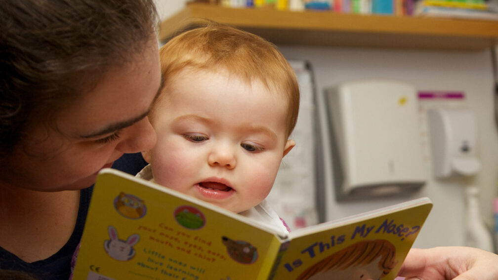 a storyteller supporting a young child with reading.