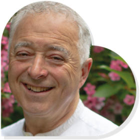 Frank Cottrell-Boyce smiling in a heart shape with foliage behind him