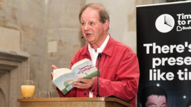 Michael presenting to an audience while holing a book.