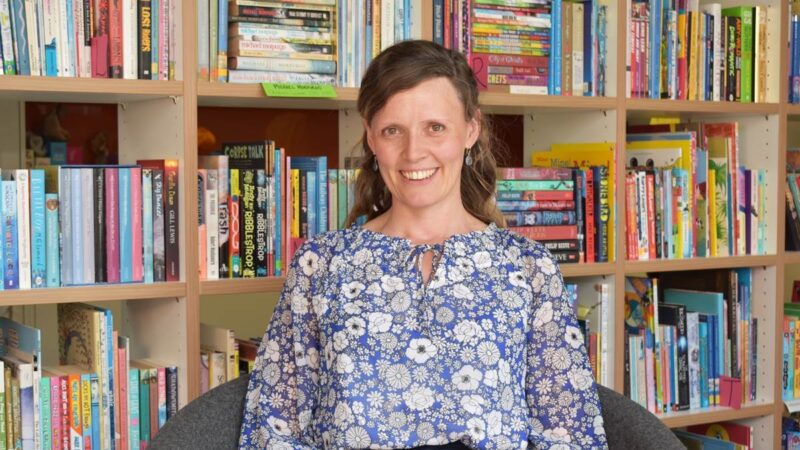 Annie, smiling to camera, with books in the background.