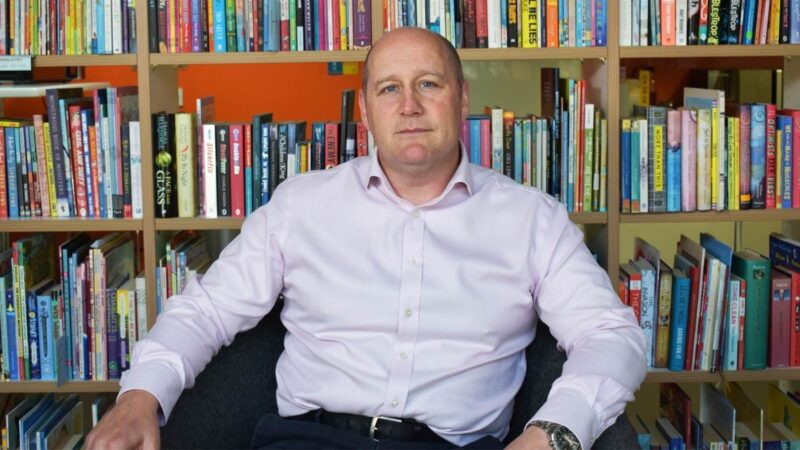 Colin looking at the camera, with books in the background.