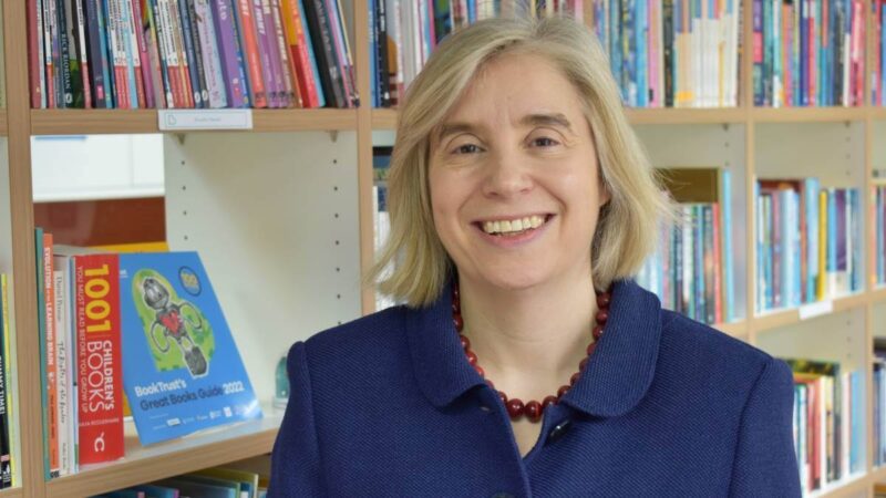 CEO of BookTrust Diana. standing in front of a bookshelf, smiling.