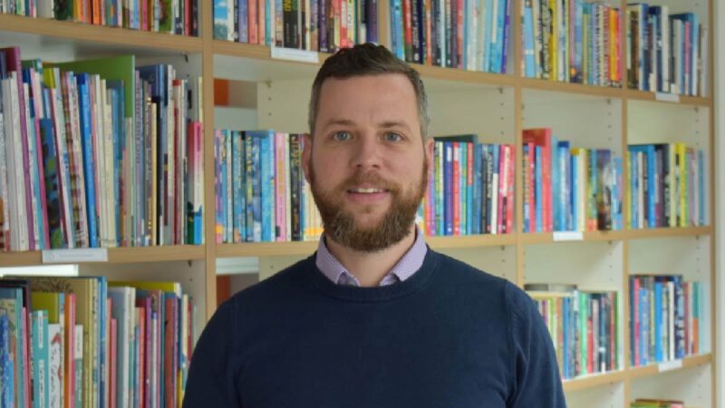 Mike smiling to camera, with books in the background.