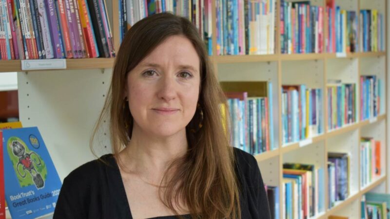 Ruthann, smiling to camera, with books in the background.